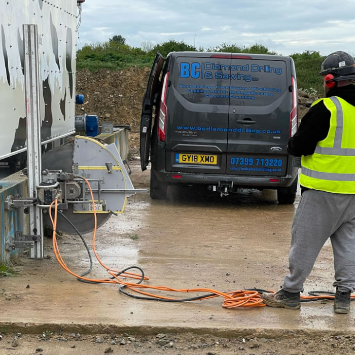 wall sawing contractor cutting a vertical hole in wall with van nearby